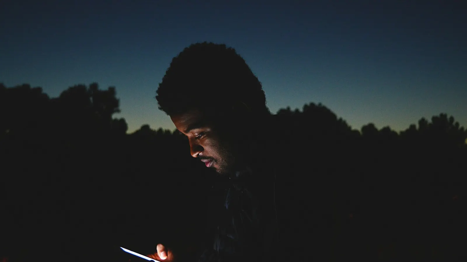 A man checking his phone outside at dusk