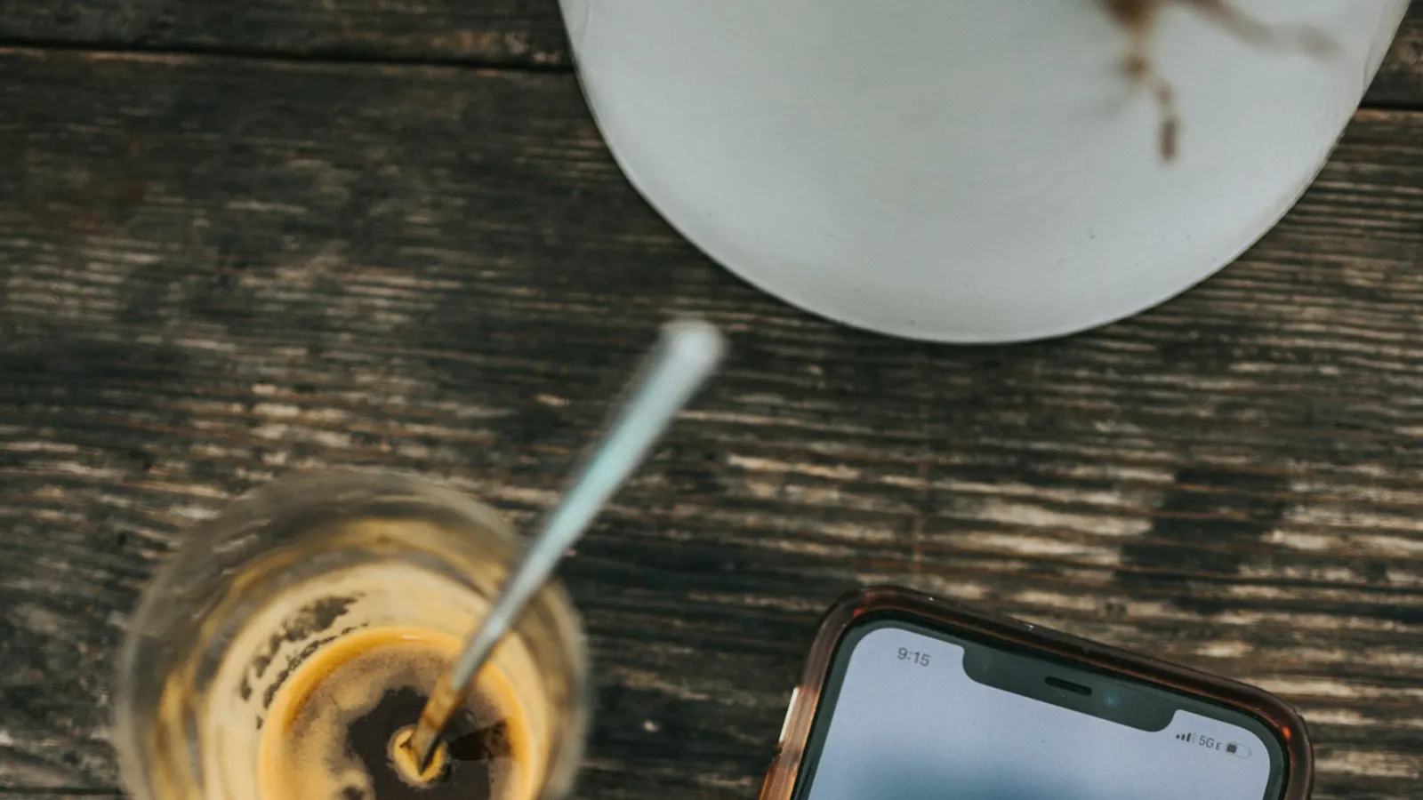 A phone showing social media apps beside a coffee on a wooden table