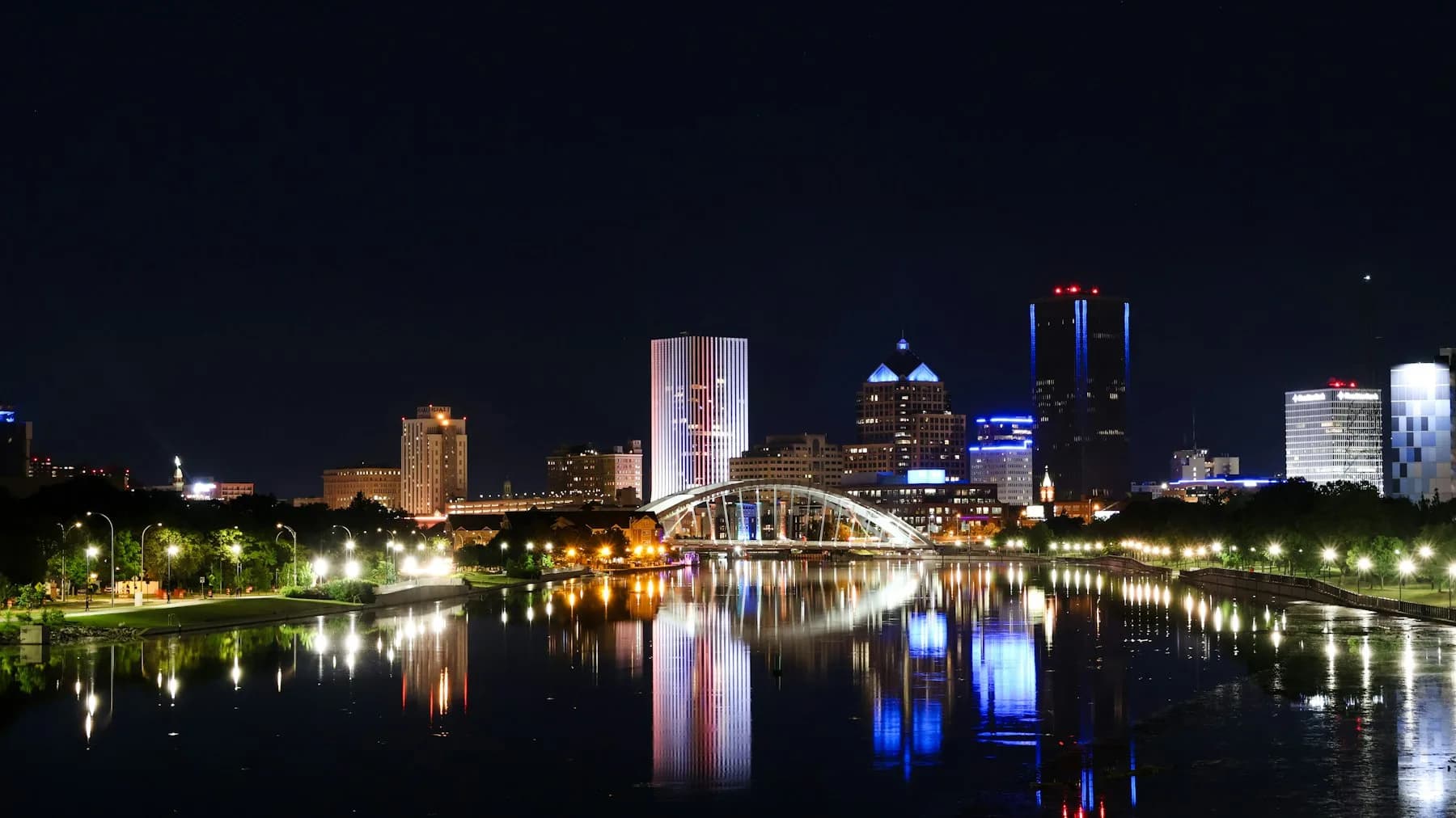 Rochester skyline lit up at night, reflected in the Genesee River
