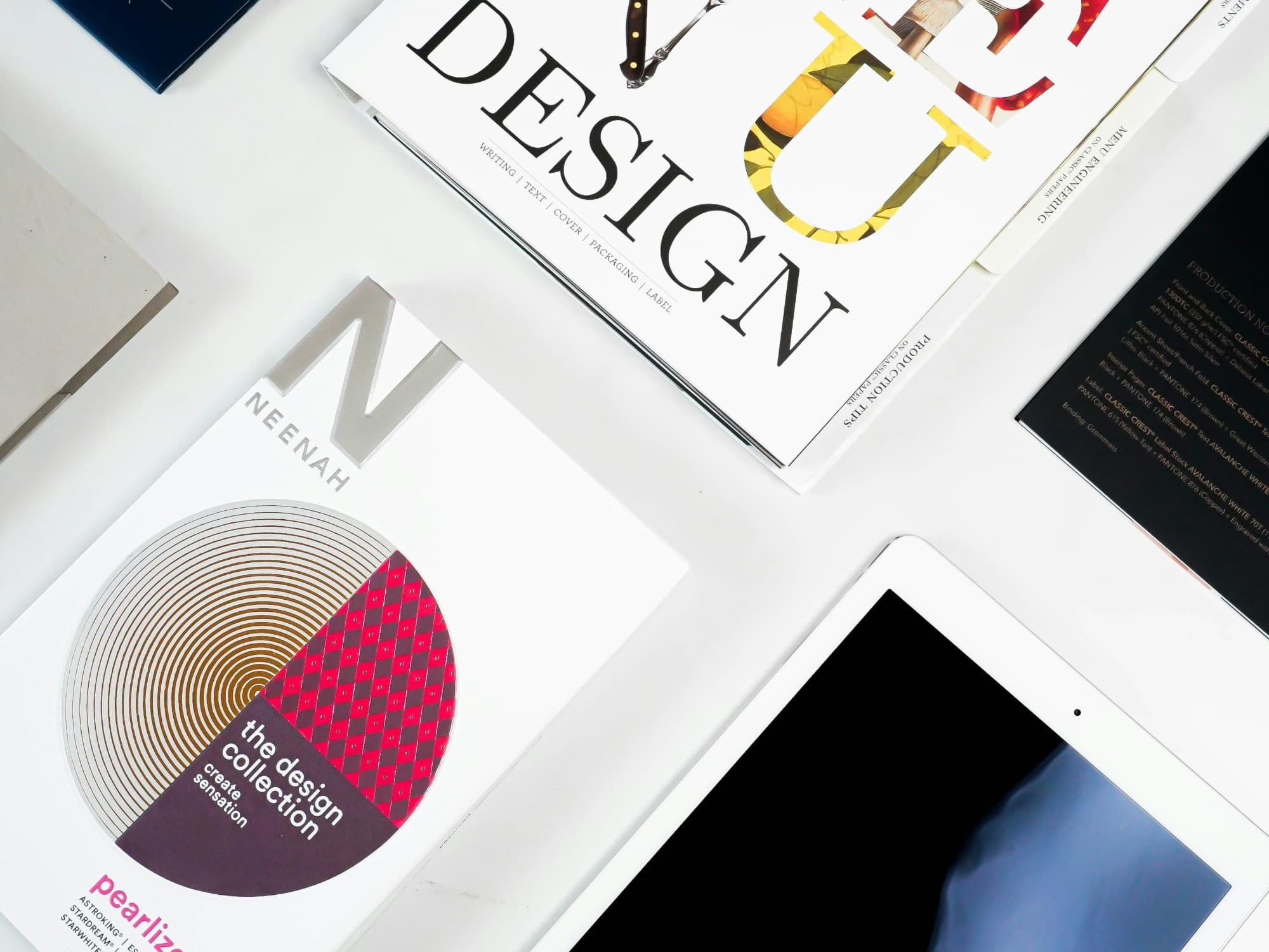 Flat lay of printed design pieces and a tablet on a white desk
