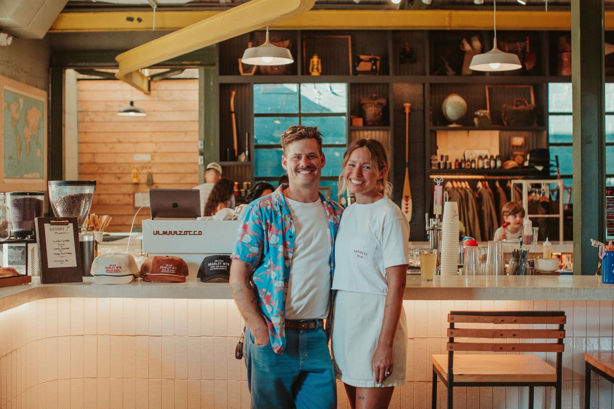 Two smiling business owners standing in front of the counter of their coffee shop