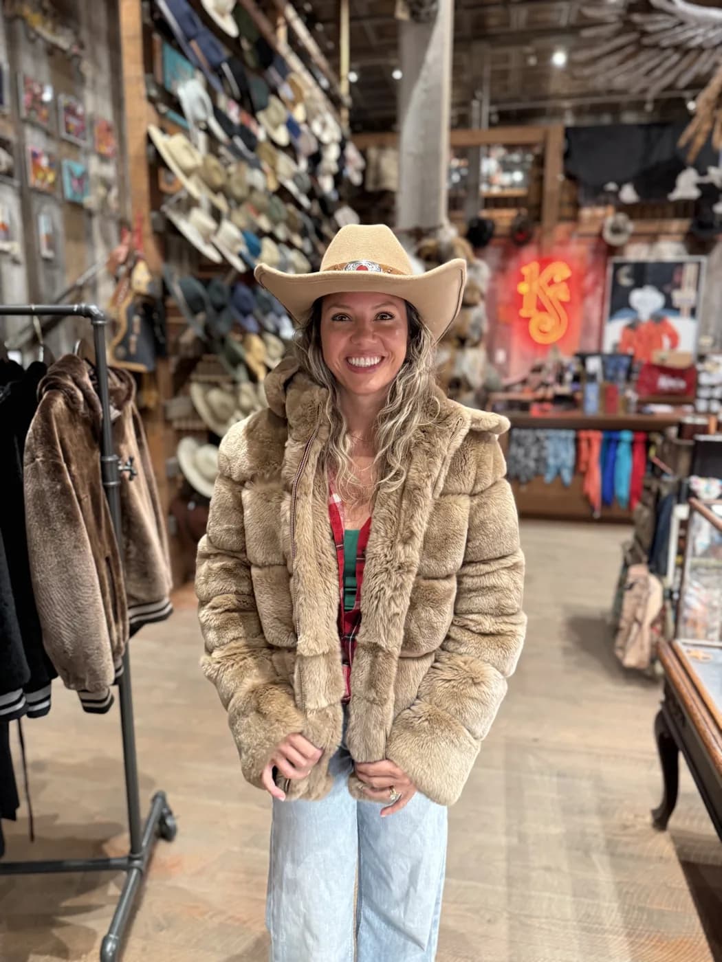 Nicole in a cowboy hat and faux-fur coat in a western hat shop