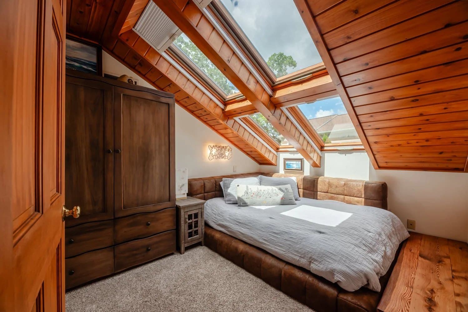 Attic bedroom with skylights, warm wood ceilings and a tufted leather bed