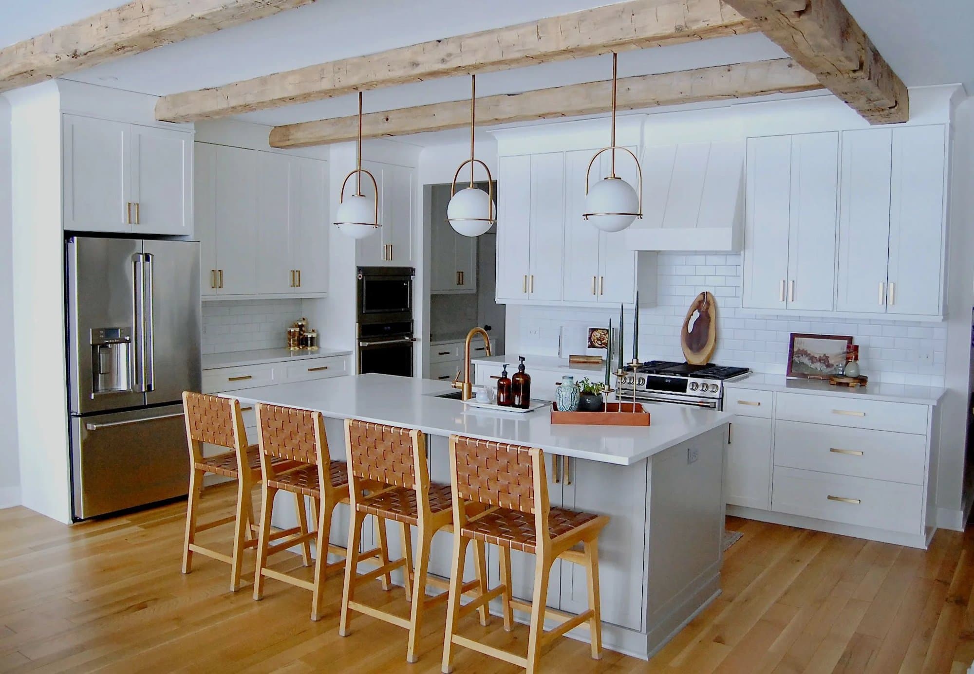 Remodeled white kitchen with reclaimed barn beams, globe pendants and a leather-stool island