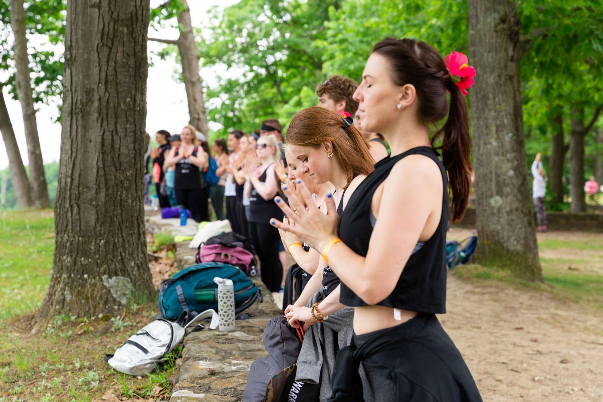 A line of attendees in quiet meditation along a stone wall