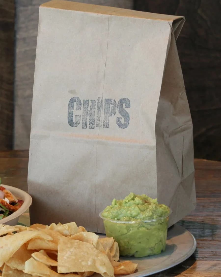 Kraft takeout bag stamped CHIPS beside a burrito bowl and guacamole